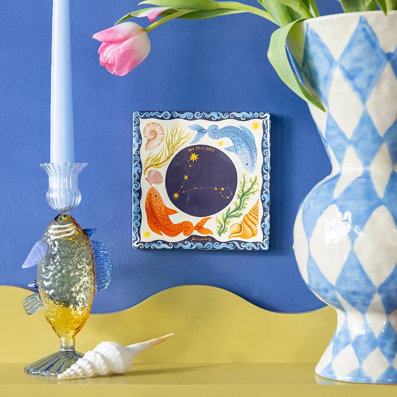 Geboortetegeltje sterrenbeeld Vissen aan blauwe muur met kaars