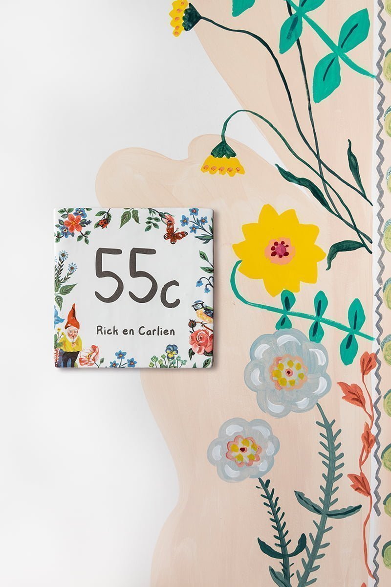 Huisnummer tegeltje met bloemmotief en kabouter, bevestigd op muur