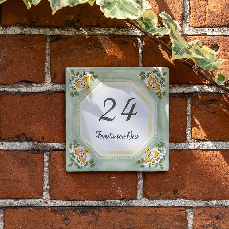 Huisnummer tegeltje met plantenmotief op bakstenen muur