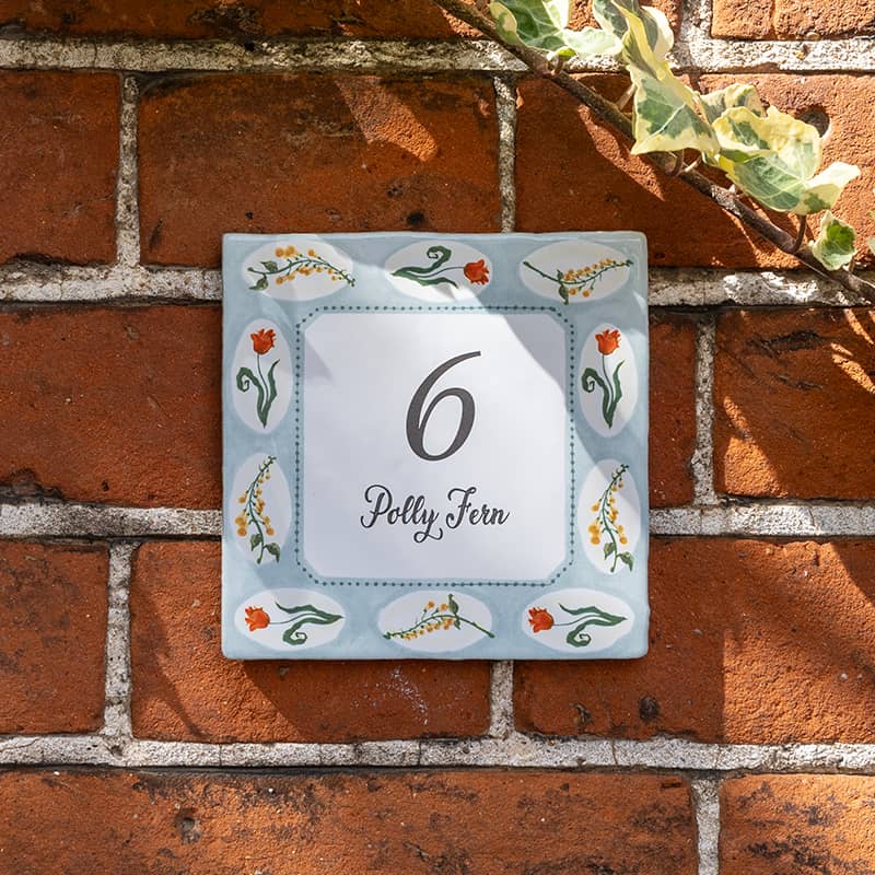 Huisnummer tegeltje met bloemen op rode bakstenen muur