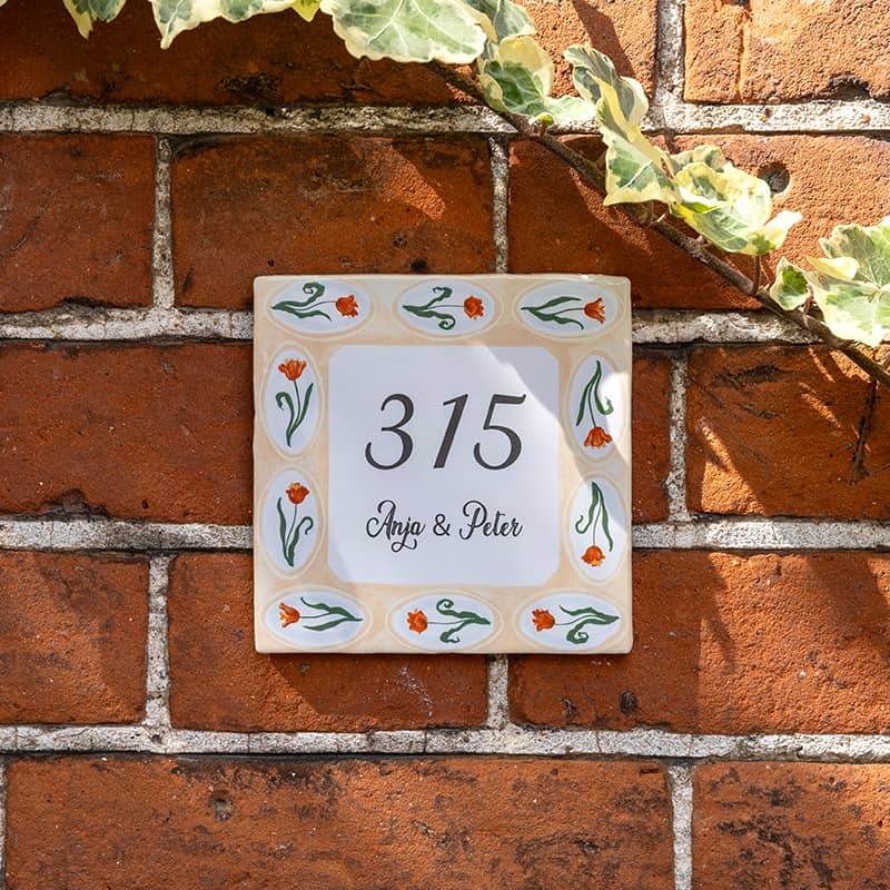 Huisnummer tegeltje met oranje bloemen op bakstenen muur