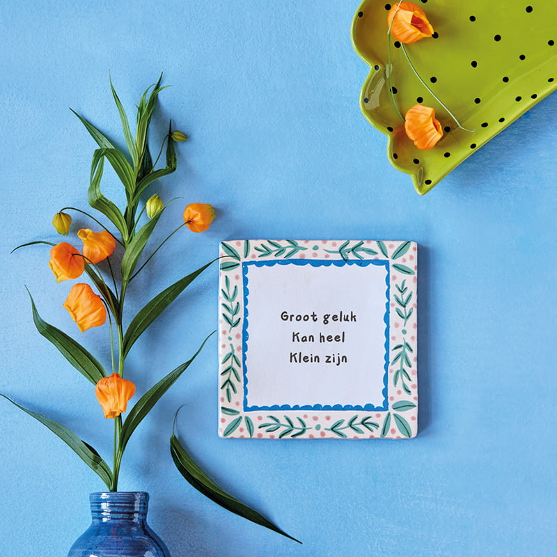 Gepersonaliseerd tegeltje met tekst en bloemen, tegen blauwe achtergrond