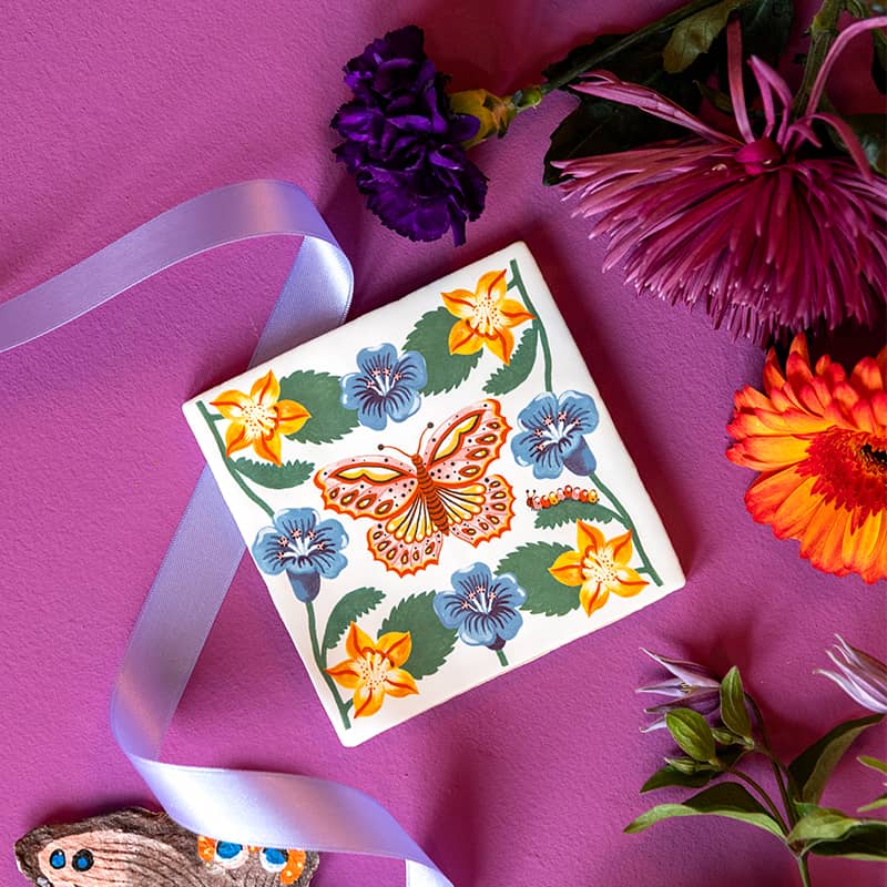 Tegeltje vlinder tussen kleurrijke bloemen op paarse achtergrond