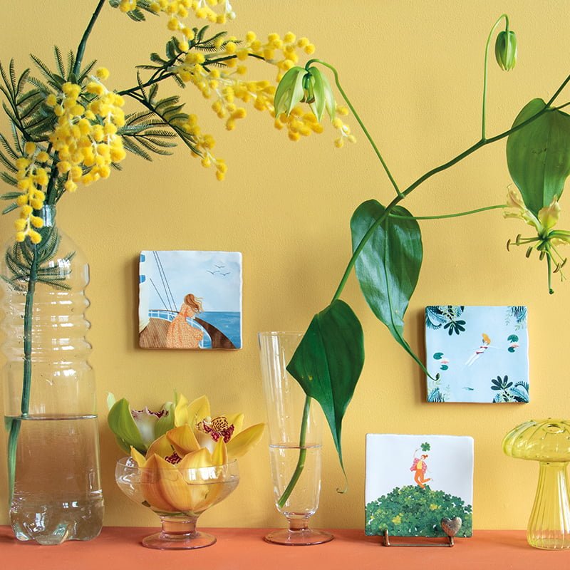 Tegeltjes met natuur- en zee-illustraties tegen een gele muur