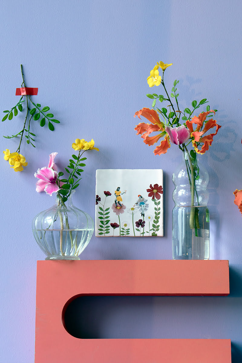 Tegeltje met twee figuren op bloemen, tegen paarse muur
