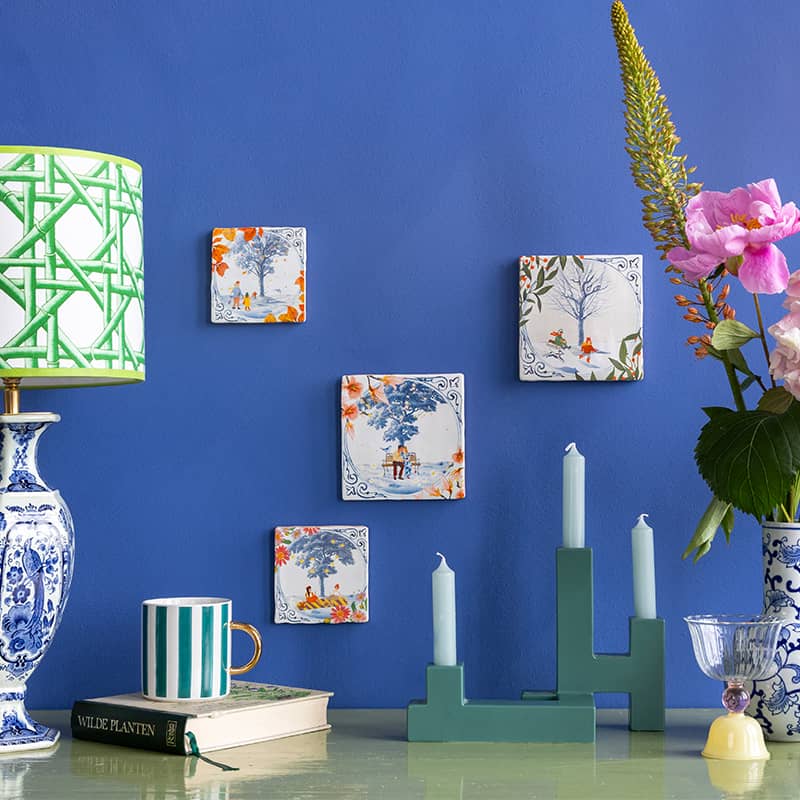 Delfts blauw tegeltje met natuurtafereel hangend op blauwe muur
