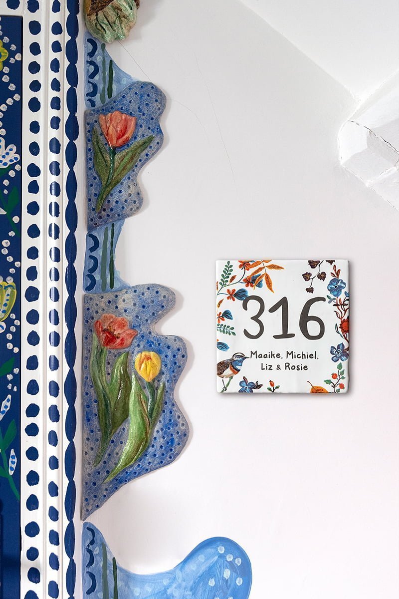 Huisnummer tegeltje met bloemen en vogeltjes aan muur bevestigd