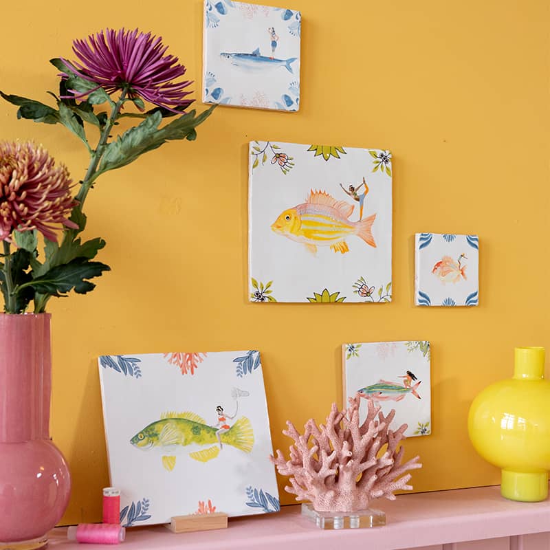 Tegeltje kleurrijke vissen aan een gele muur met bloemen