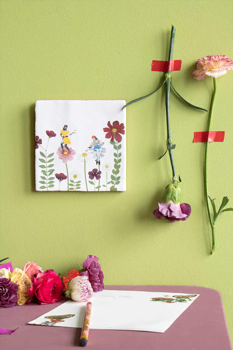 Tegeltje met bloemen en figuurtjes aan groene muur
