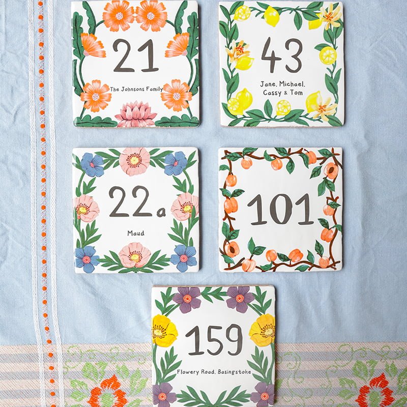 Huisnummer tegeltjes met kleurrijke bloemenranden op een tafelkleed