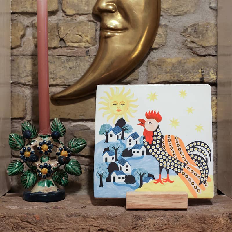 Tegeltje haan, dorpshuisjes, zon, op bakstenen achtergrond met decoraties