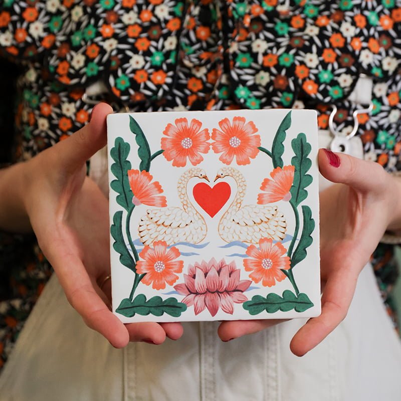 Gepersonaliseerd tegeltje met zwanen en bloemen, vastgehouden door handen