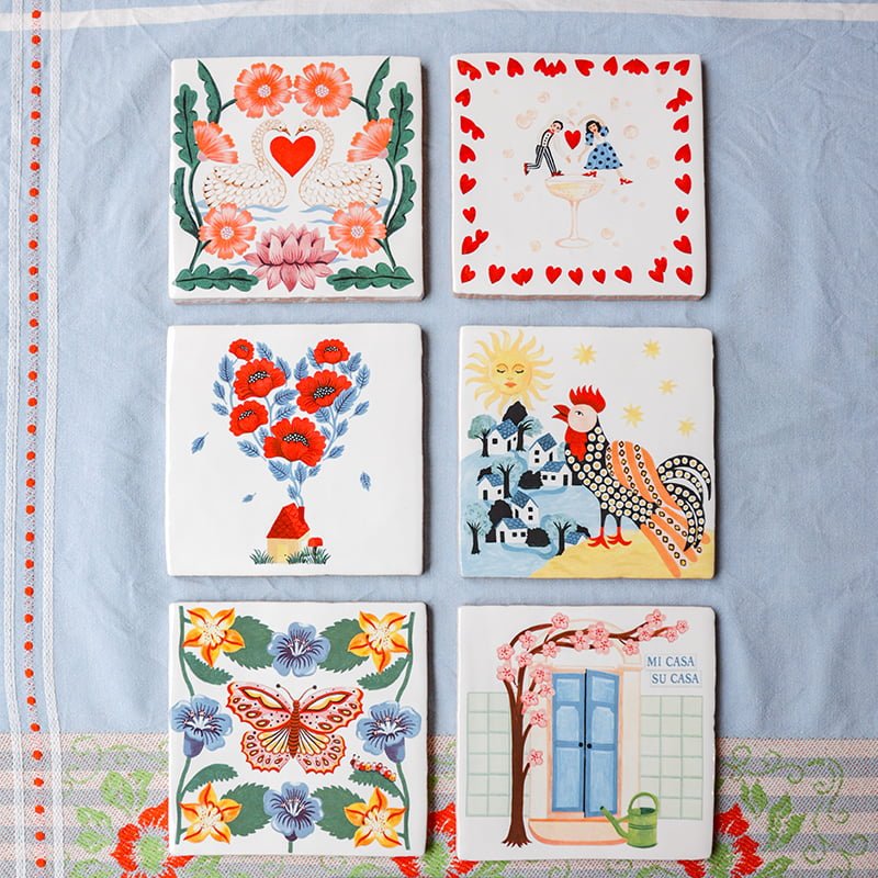 Zes gepersonaliseerde tegeltjes met kleurrijke illustraties op een tafelkleed