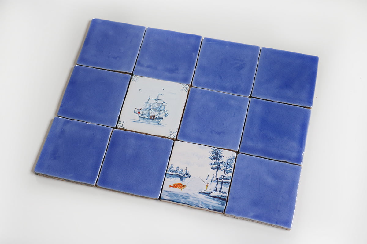 Blauw tegeltableau met scènes van schip en visser, centraal geplaatst