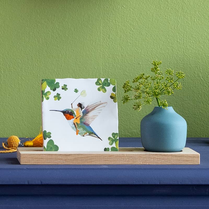 Tegeltje met elfje op vogel, geplaatst naast blauwe vaas