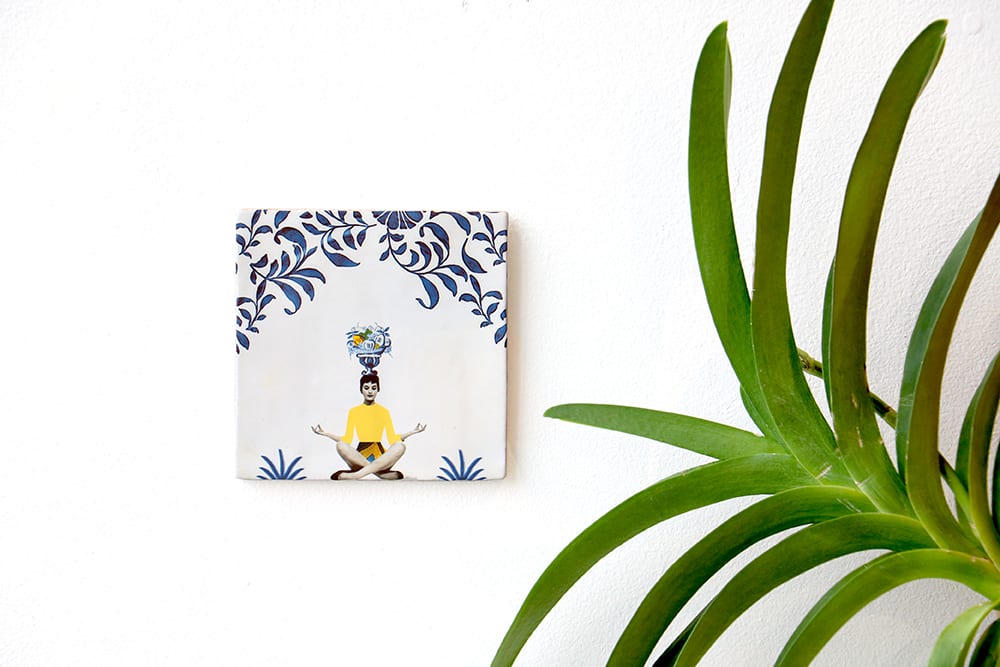 Tegeltje met yogafiguur en florale decoratie aan witte muur