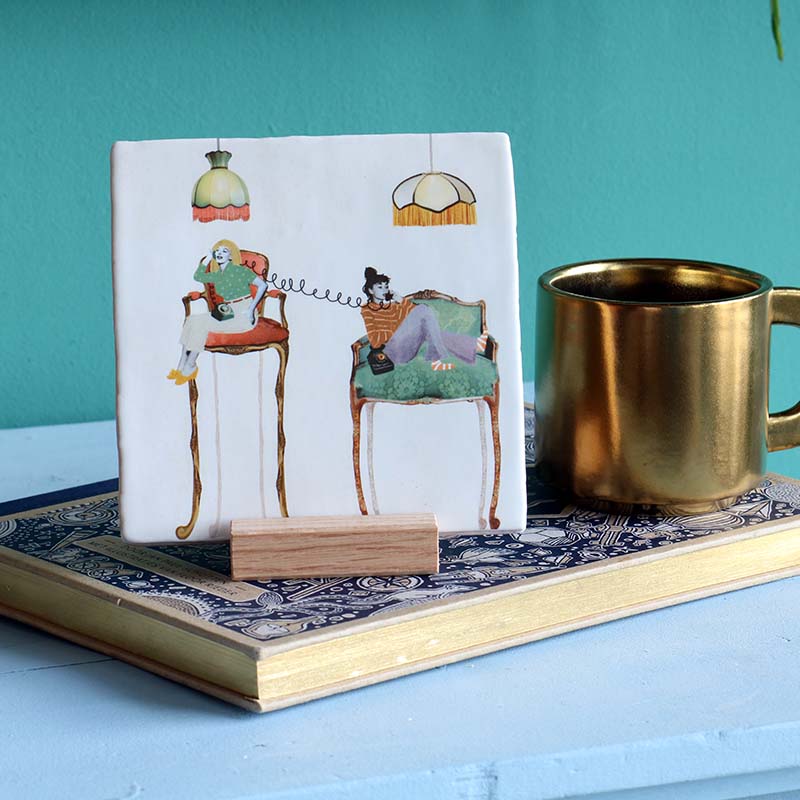 Tegeltje telefonerend duo op stoelen, naast gouden mok