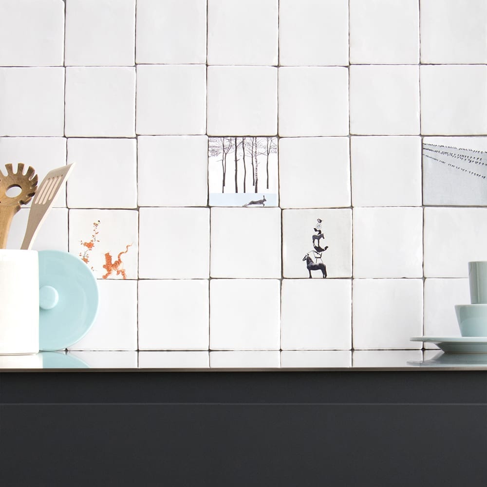 Witte tegels met illustraties aan een keukenmuur boven aanrecht