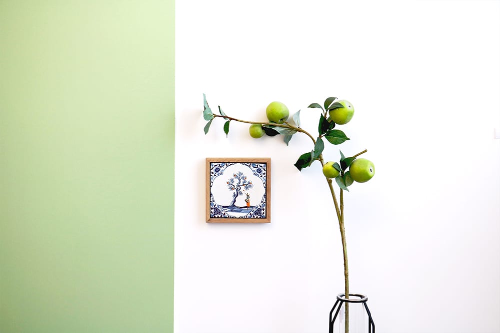 Tegeltje met boom naast groene muur en tak met appels