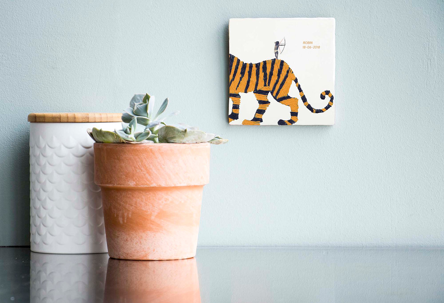 Tegeltje met tijger en boogschutter aan wand, planten ernaast