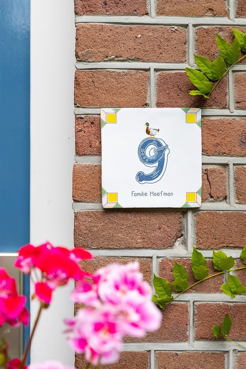 Huisnummer tegeltje met eend op bakstenen muur en bloemen