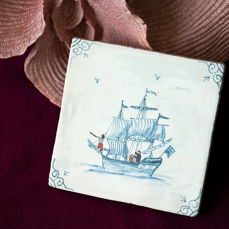 Delfts blauw tegeltje met zeilschip, gepresenteerd op wijnrode achtergrond