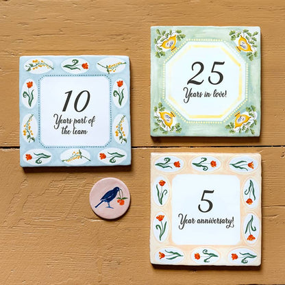 Jubileumcadeau tegeltje met jaartal en bloemenmotief op tafel