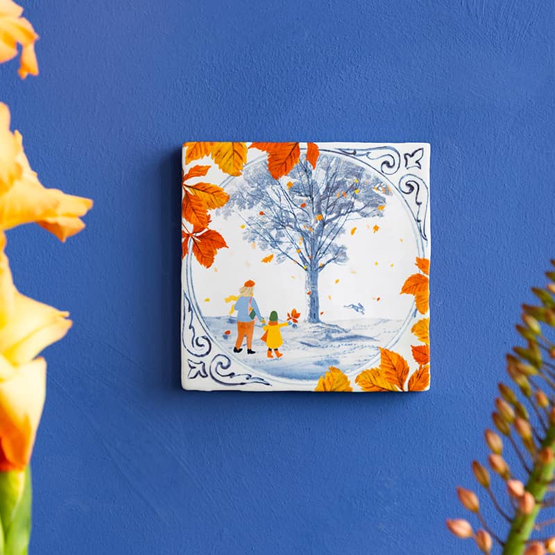 Delfts blauw tegeltje met herfstscène van boom en bladeren aan muur