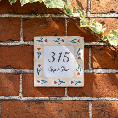 Huisnummer tegeltje met oranje bloemen op bakstenen muur