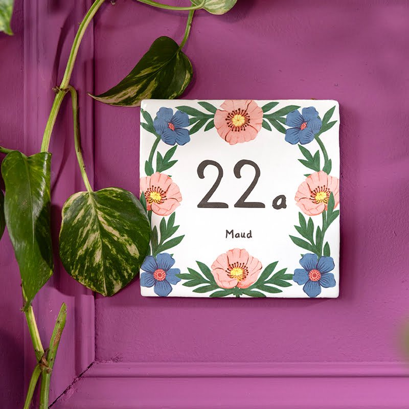 Huisnummer tegeltje met bloemenrand tegen paarse achtergrond en bladeren