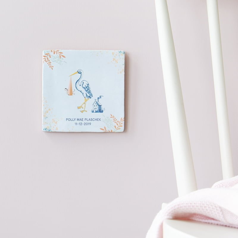 Geboortetegel ooievaar met baby aan pastelroze muur bevestigd
