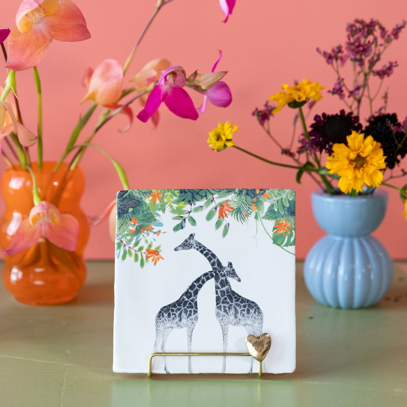 Tegeltje met giraffen, omlijst door bloemen en bladeren