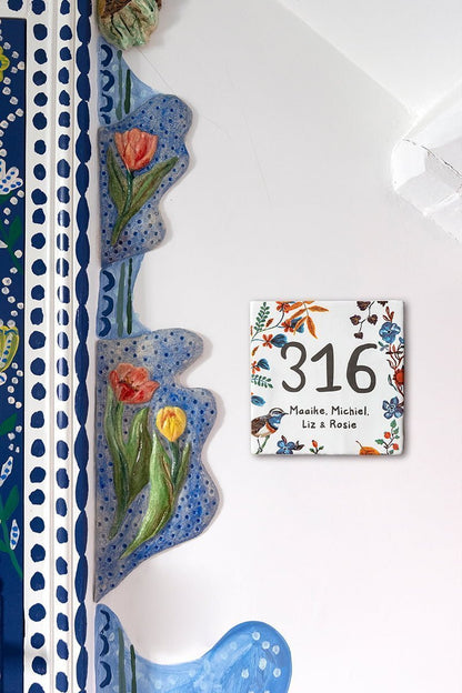 Huisnummer tegeltje met bloemen en vogeltjes aan muur bevestigd