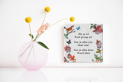 Tegeltje met tekst, bloemen en vogels aan witte muur