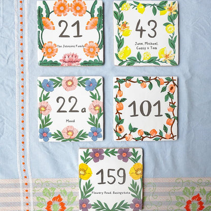 Huisnummer tegeltjes met kleurrijke bloemenranden op een tafelkleed