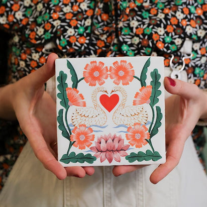 Gepersonaliseerd tegeltje met zwanen en bloemen, vastgehouden door handen