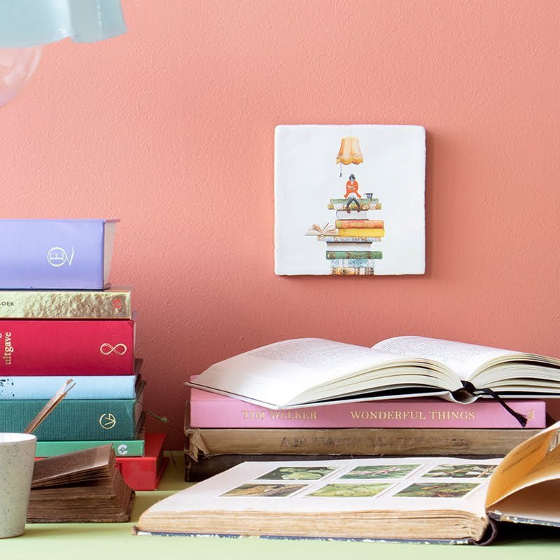 Geslaagd cadeau tegeltje vrouw op boekenstapel aan roze muur