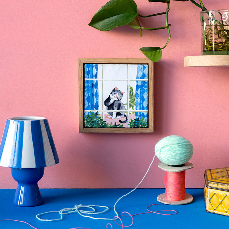 Tegeltje kat die zich wast in een houten lijst