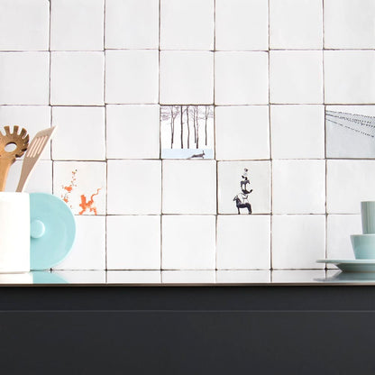 Witte tegels met illustraties aan een keukenmuur boven aanrecht