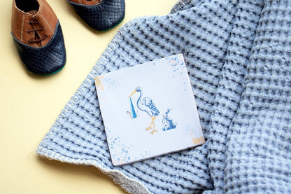 Geboortetegel ooievaar op blauwe deken met babyschoentjes