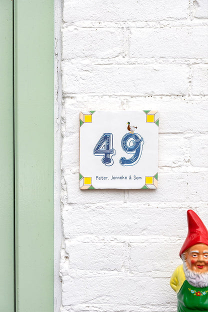 Huisnummer tegeltje met eend op witte bakstenen muur