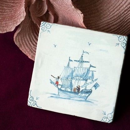 Delfts blauw tegeltje met zeilschip, gepresenteerd op wijnrode achtergrond