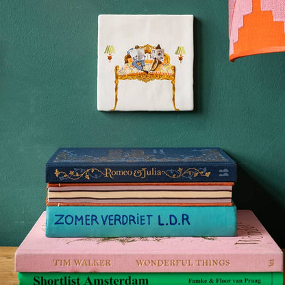 Huwelijkscadeau of liefdescadeau tegeltje met illustratie bed met lezend koppel, opgehangen boven gestapelde boeken 