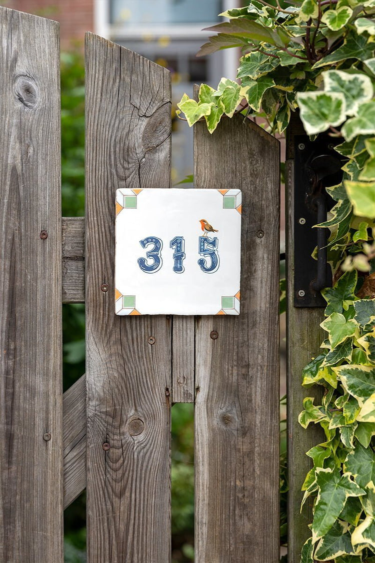 Huisnummer tegeltje met vogel, omringd door houten hek