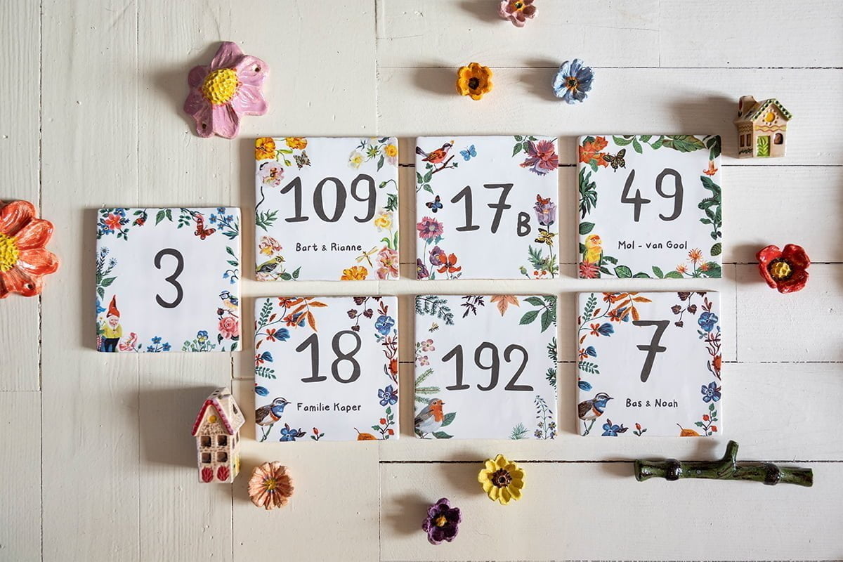 Huisnummer tegeltjes met kleurrijke bloemenrand naast decoratieve bloemen