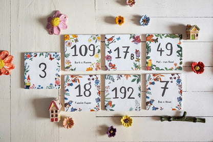 Huisnummer tegeltjes met kleurrijke bloemenrand naast decoratieve bloemen