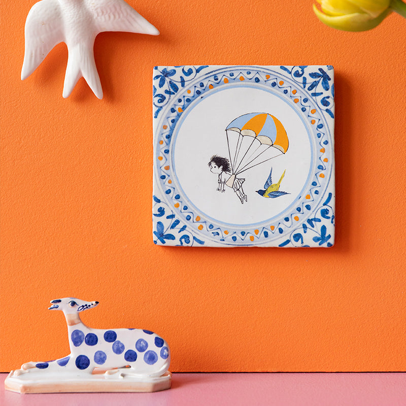 Fiep Westendorp kindertegeltje met meisje zwevend aan parachute opgehangen aan een oranje muur