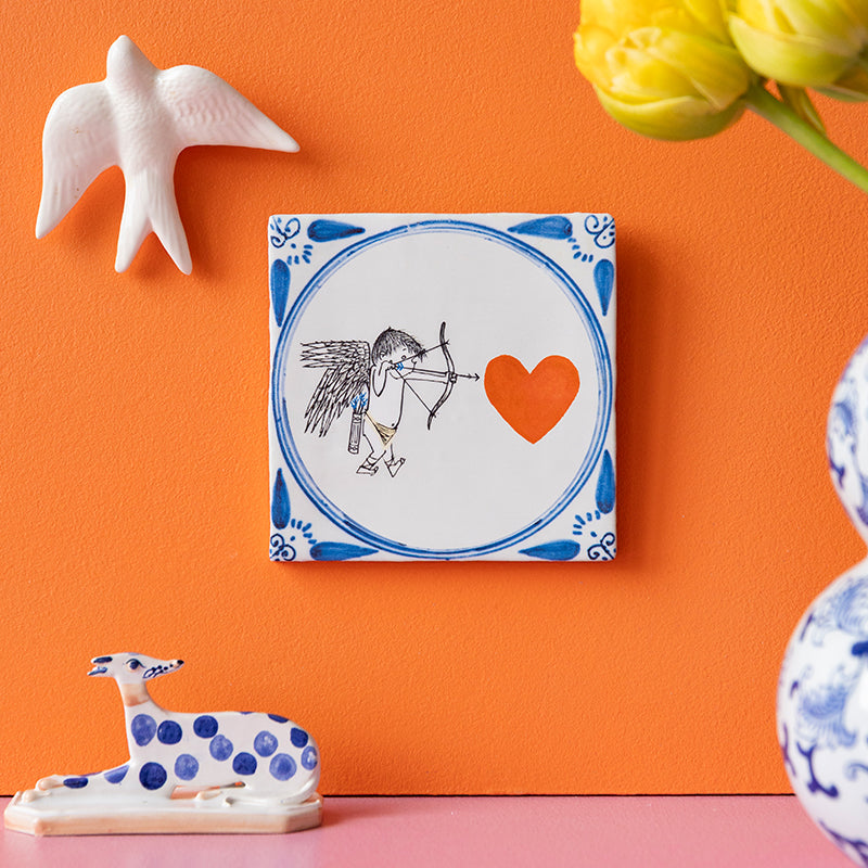 tegeltje met cupido van Fiep Westendorp aan oranje muur