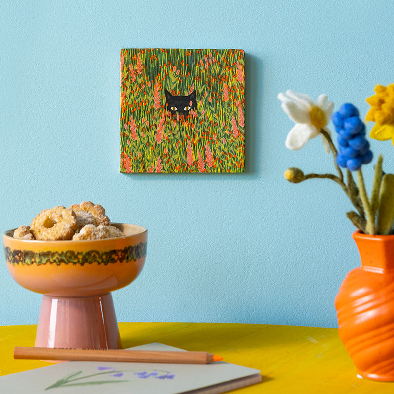 Tegeltje met zwarte kat die kopje boven een bloemenveld uitsteekt