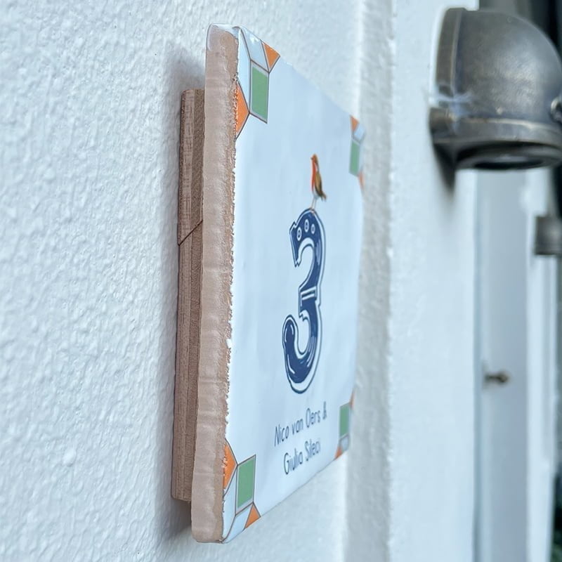 Huisnummer tegeltje op muur opgehangen met ophangplaatje